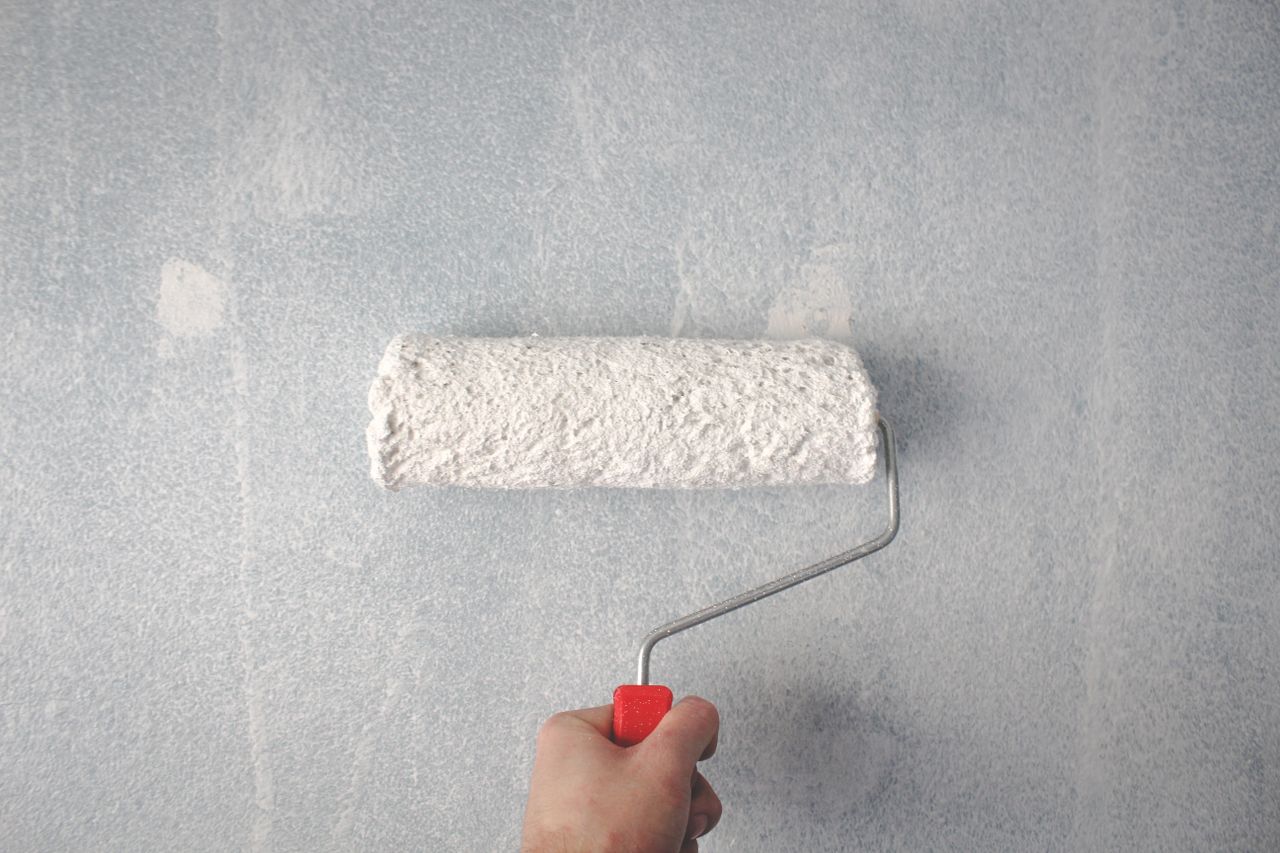 home-img A person's hand using a paint roller to apply white paint on a wall.