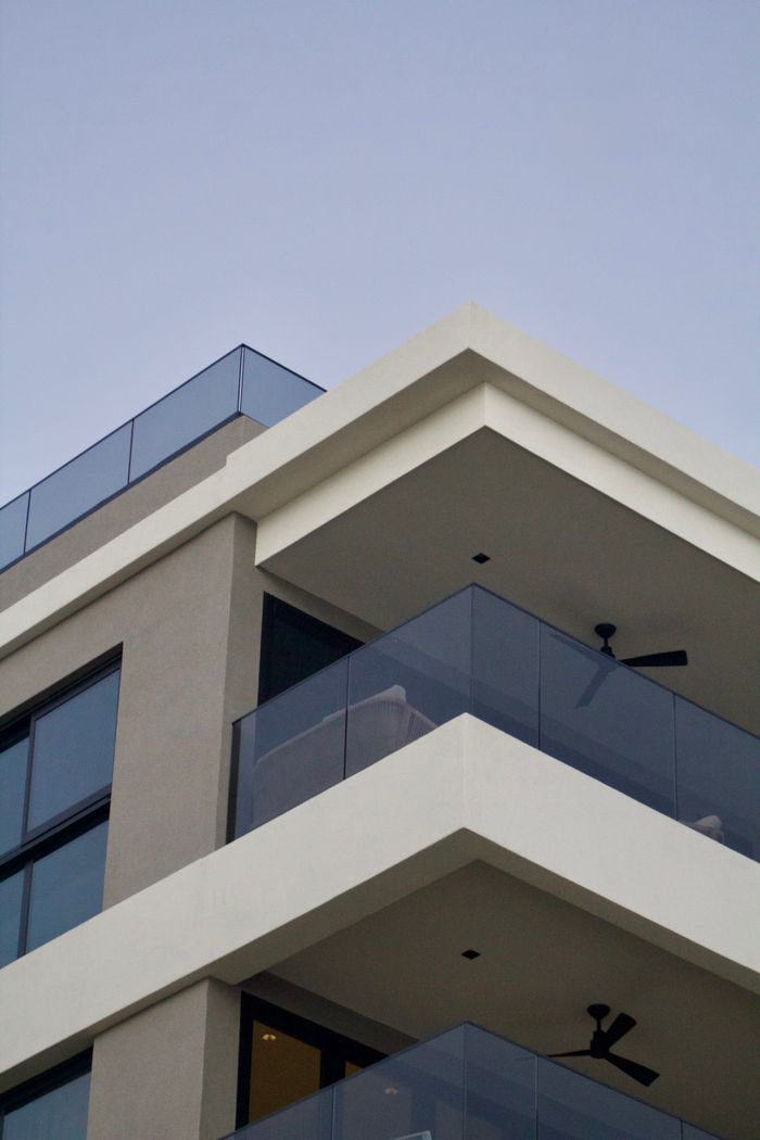 gallery-04 Contemporary apartment building with glass balconies against a clear sky.
