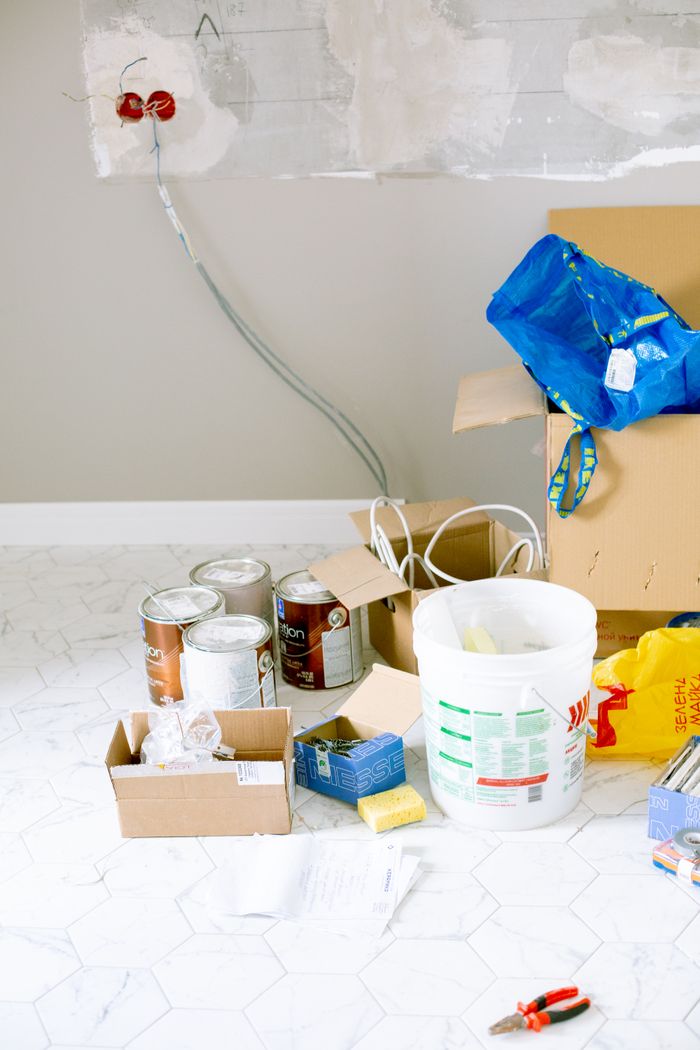 gallery-01 A cluttered room with renovation supplies including paint cans, boxes, and tools.