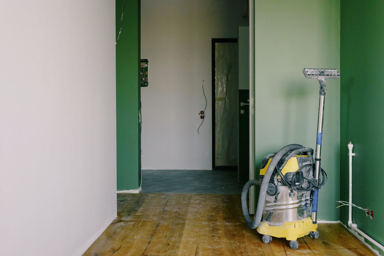 gallery-03 Industrial vacuum cleaner placed on dirty parquet in room with green walls and doorway in spacious apartment during repair works