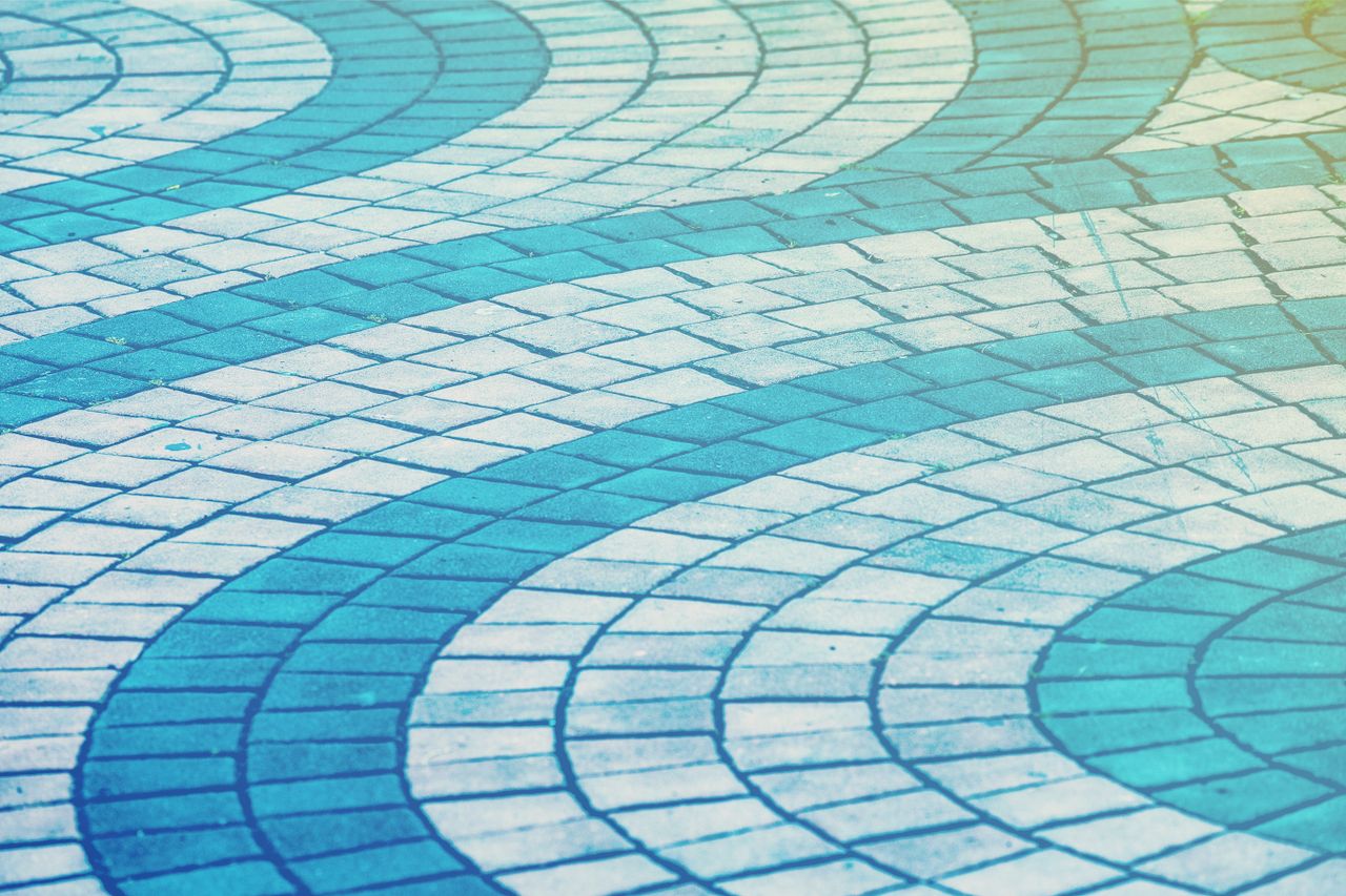 services-02 Curved blue and white paving tiles forming an abstract wave pattern on a walkway.
