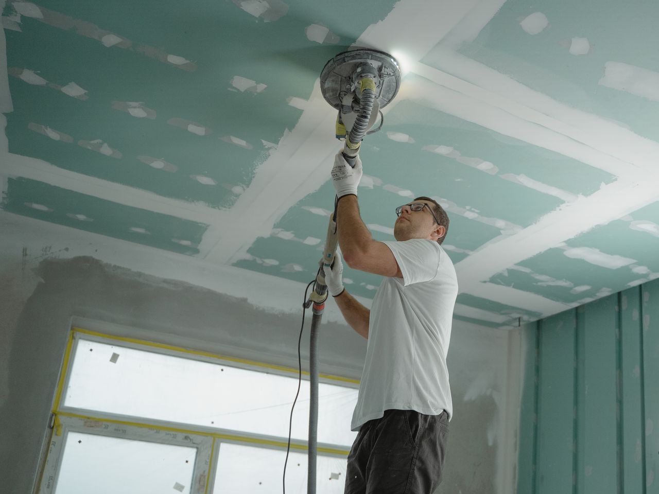 gallery-02 A professional worker sanding the ceiling during a home renovation project. Indoor construction setting.