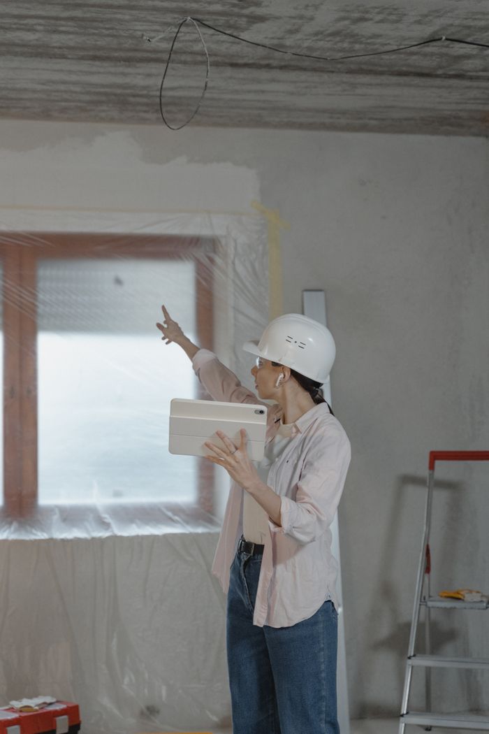 journey-02 Woman in hard hat using tablet to oversee home renovation in a partially completed room.
